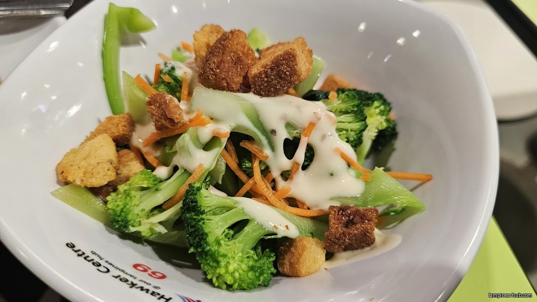 A bowl of salad with broccoli, carrots, croutons, and creamy dressing.