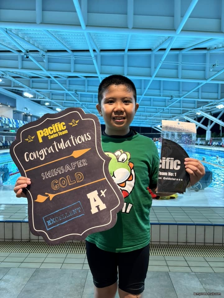 Boy holding a congratulations sign and swim gear at a pool.