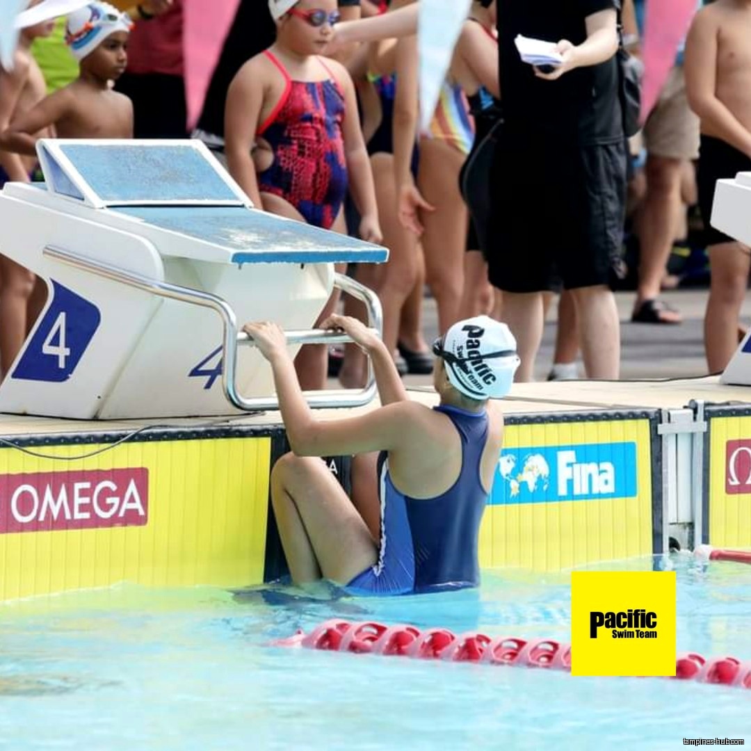 Swimmer in the pool with starting block and other swimmers nearby.