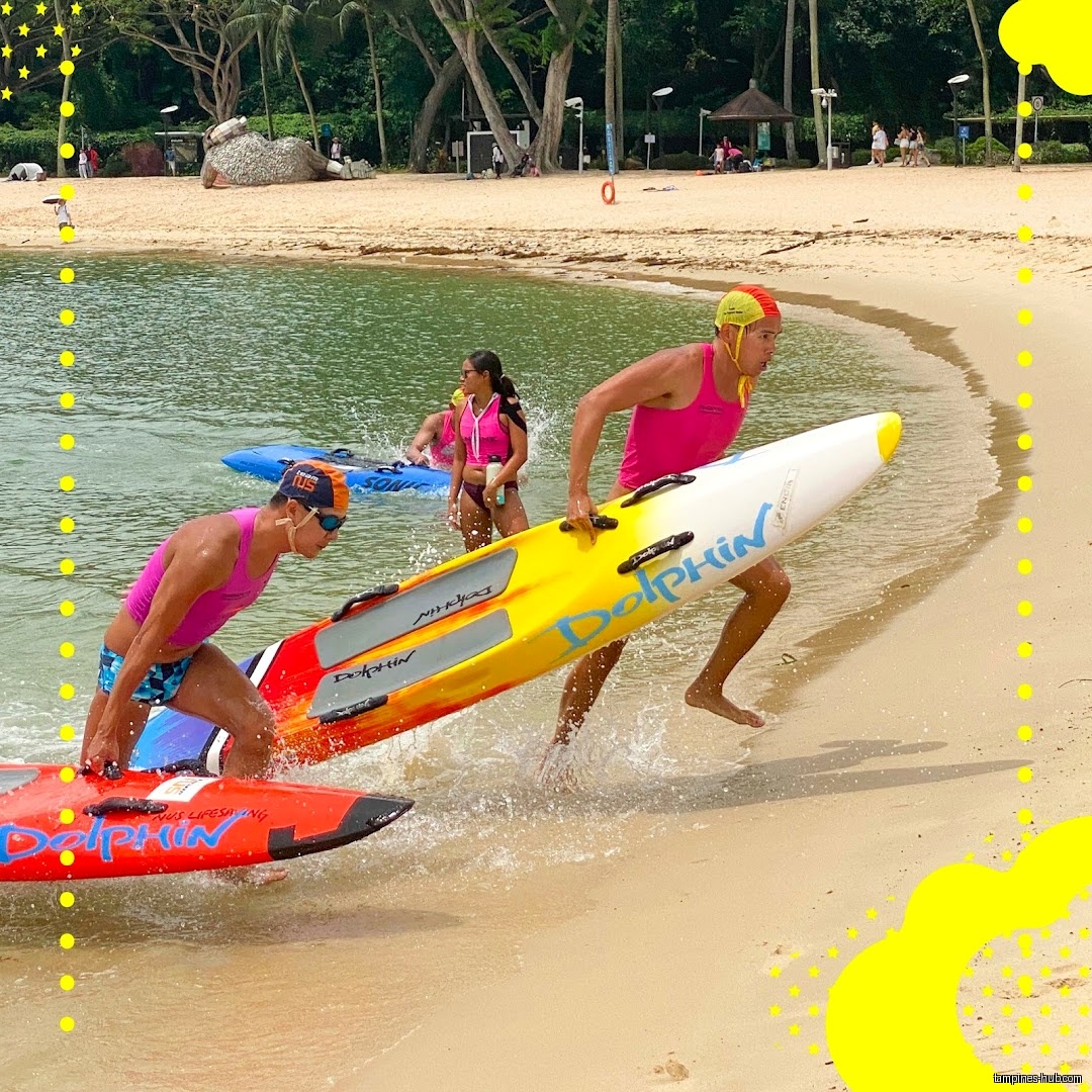 Lifeguards in pink shirts run on the beach with rescue boards.