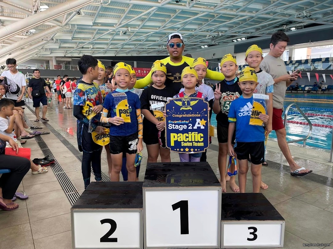 Children on a podium holding a Pacific Swim Team sign near a pool.