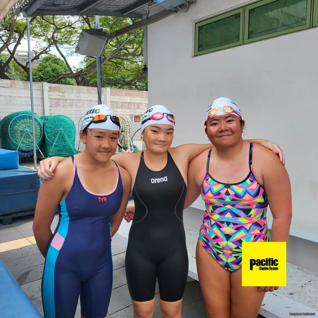 Three young swimmers in swimsuits and caps pose together for a photo.