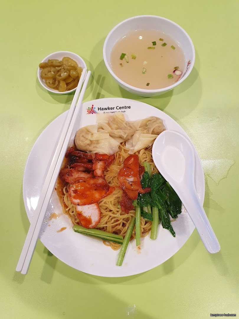 Overhead shot of a plate of wanton noodles with soup and pickled peppers.
