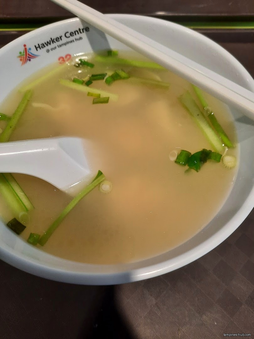 A bowl of soup with green onions, a spoon, and chopsticks.