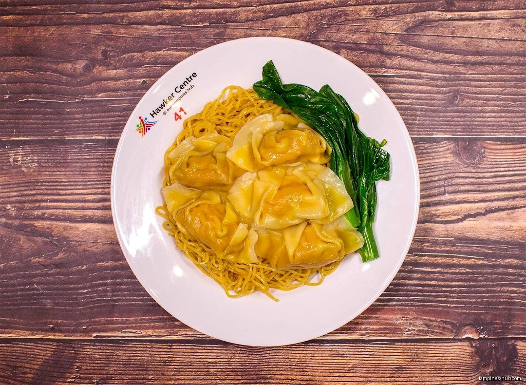 A plate of wanton noodles with vegetables on a wooden table.