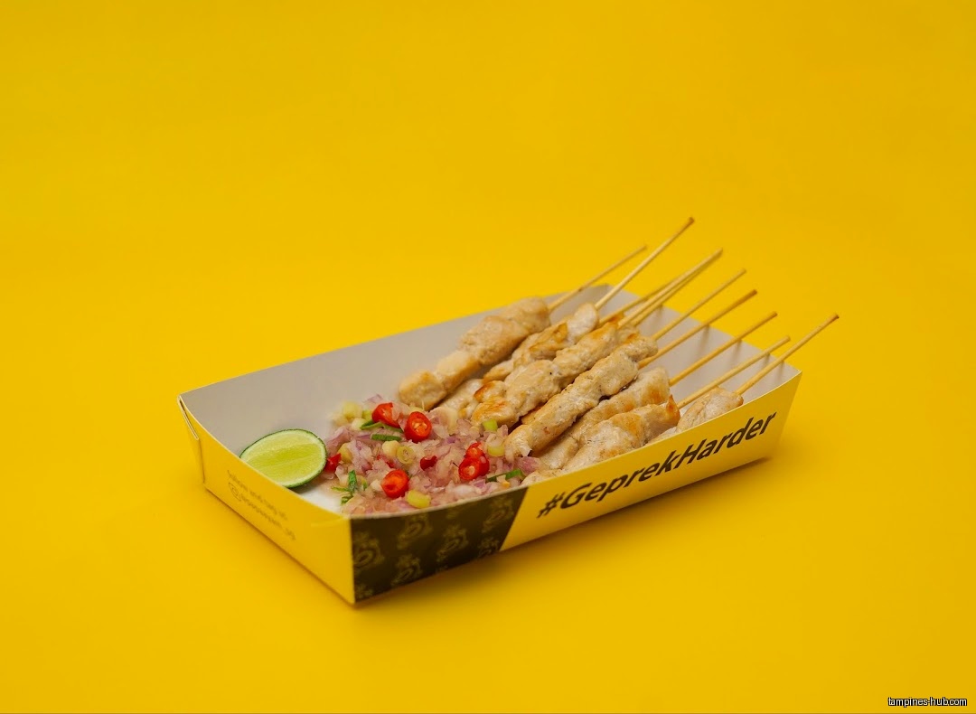 Chicken satay skewers with sambal and lime on a yellow background.