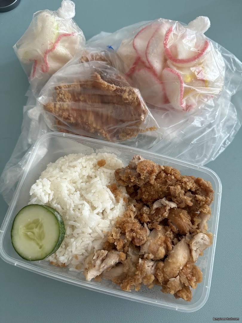 A container of rice and fried chicken with side dishes.