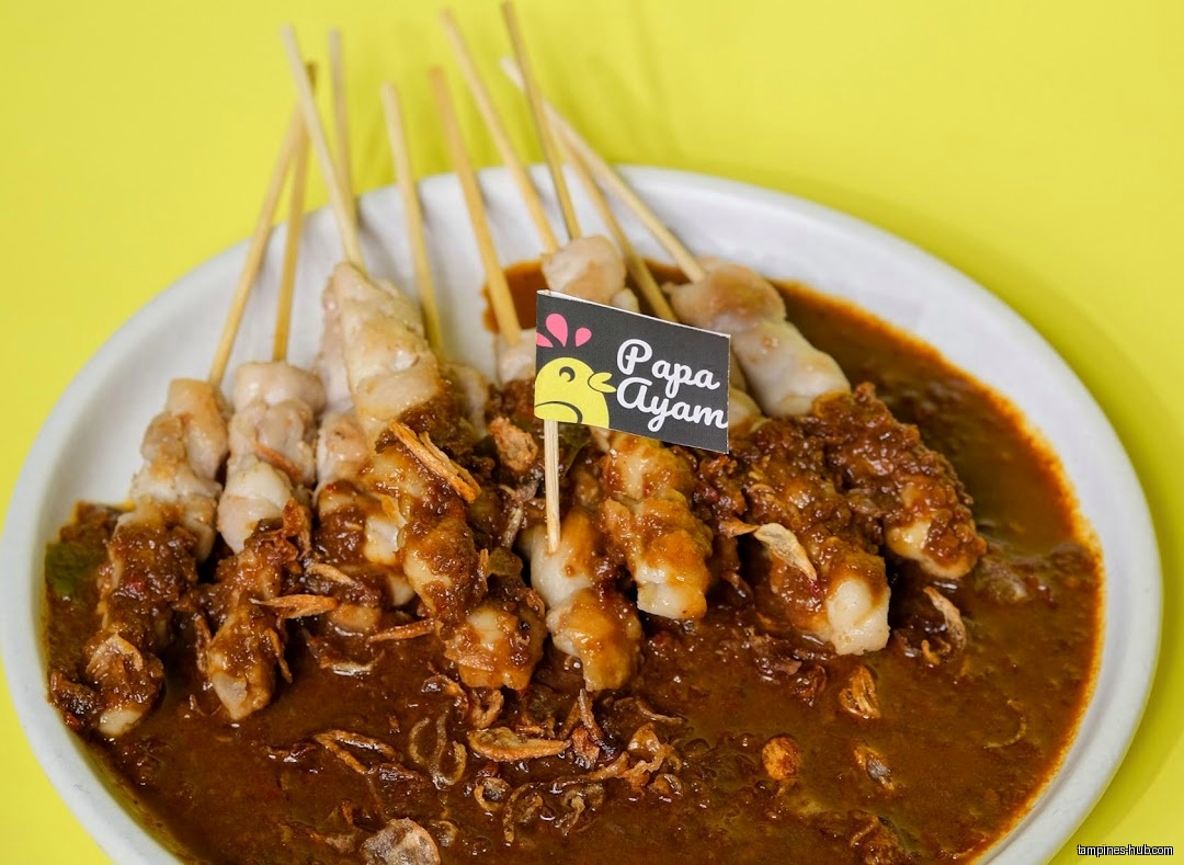 A plate of Papa Ayam chicken satay with peanut sauce is shown.