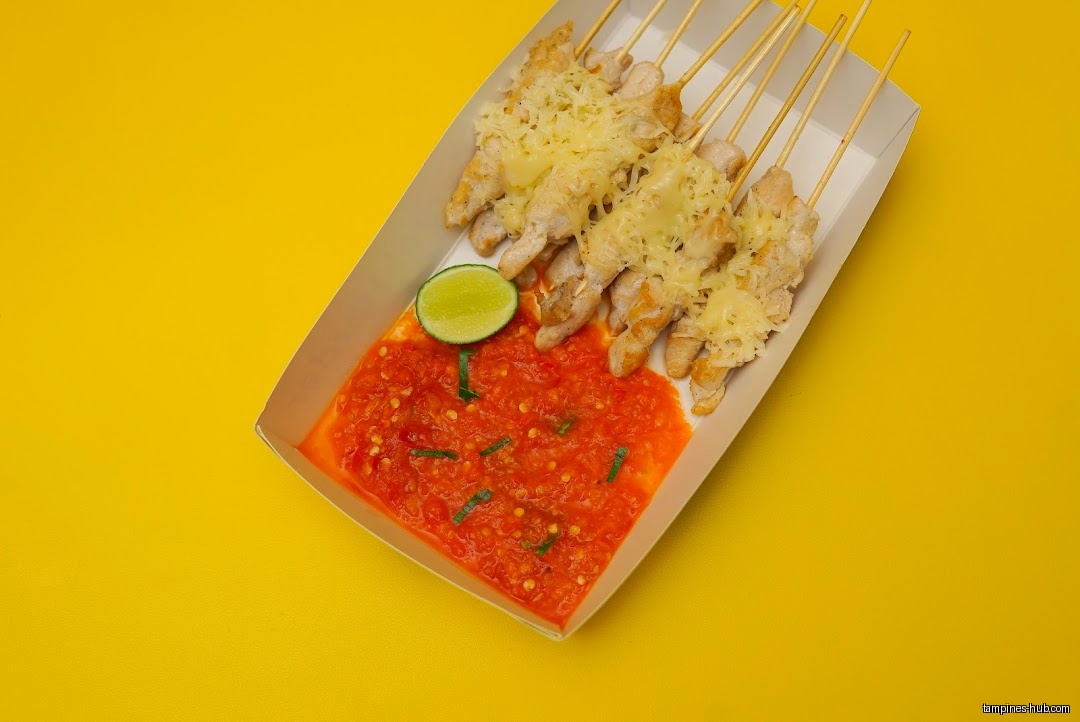 Chicken satay with cheese, chili sauce, and lime on a yellow background.