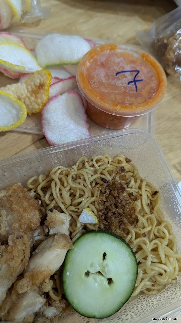 A container of noodles, fried chicken, cucumber, crackers, and chili sauce.