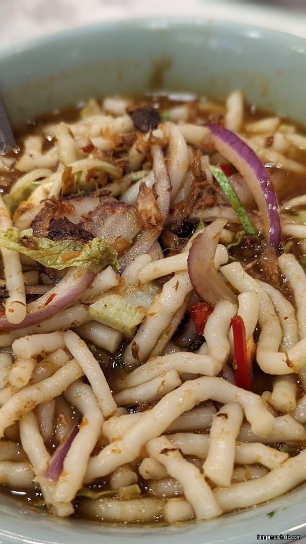 A close-up shot of a bowl of Penang Laksa with thick noodles.