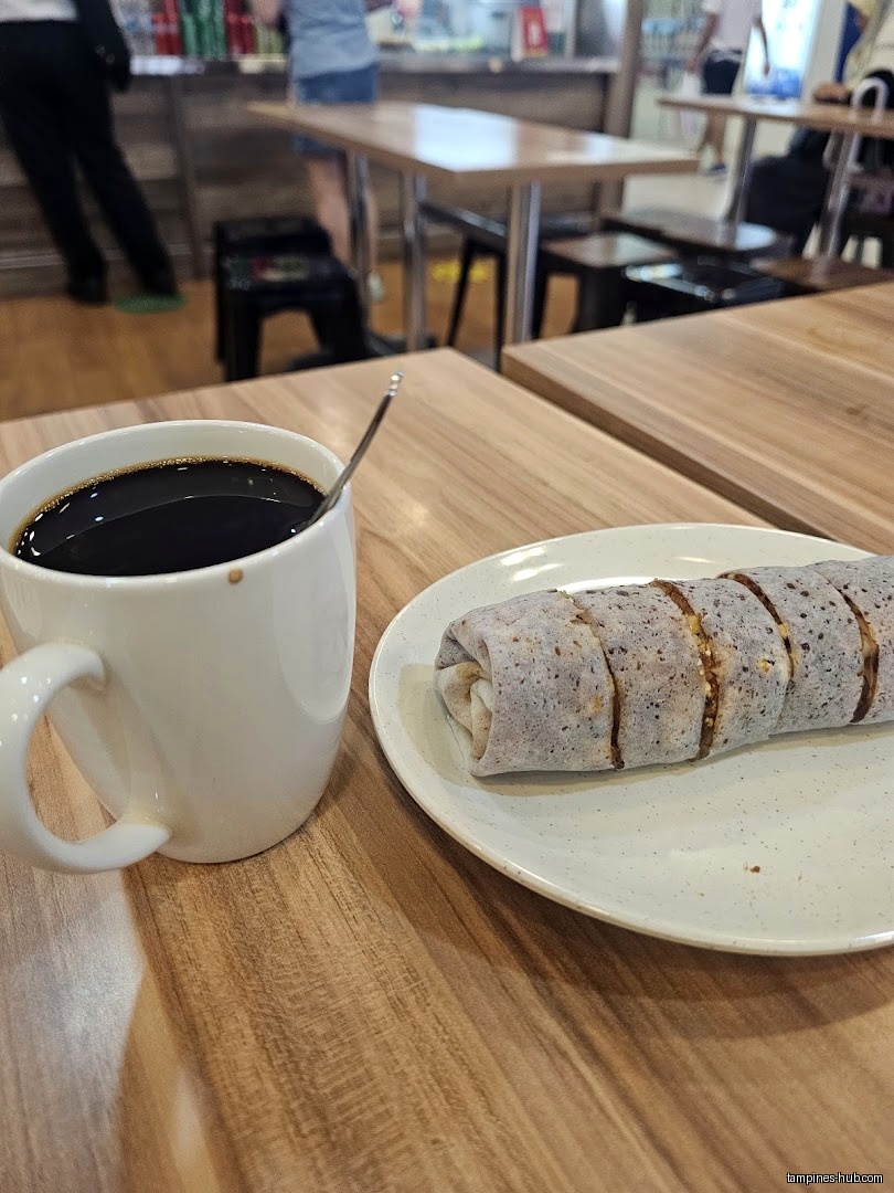 A cup of coffee and a popiah roll on a plate on a table.