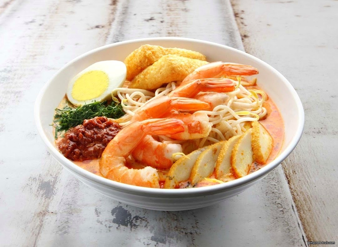 A bowl of laksa with prawns, egg, and other ingredients.
