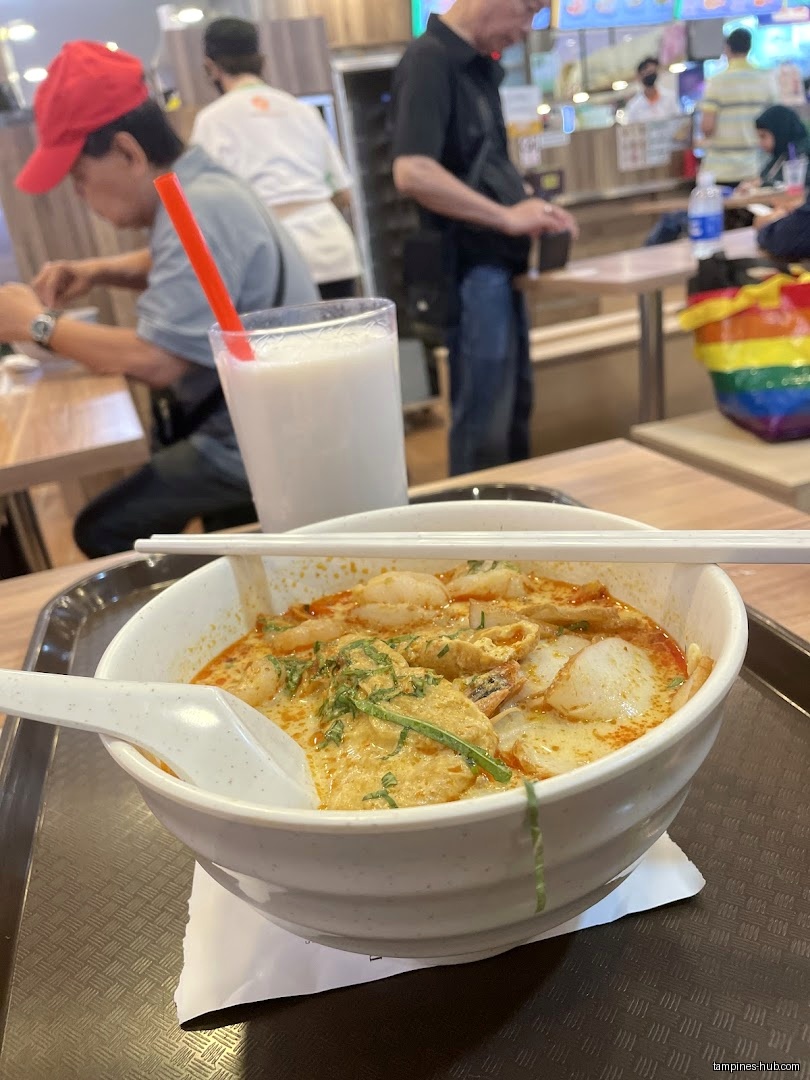 A bowl of laksa and a drink are on a tray in a restaurant.