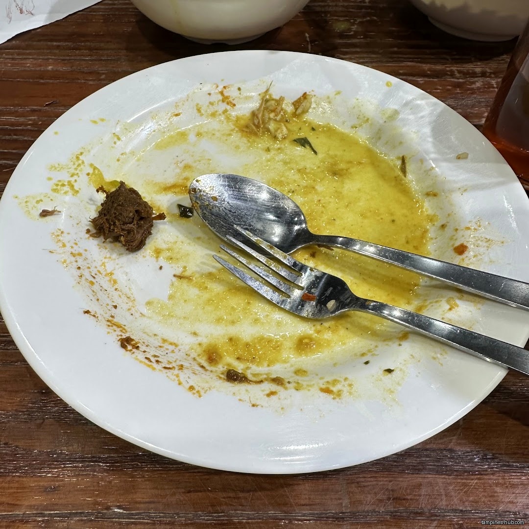 A dirty white plate with leftover food and cutlery on a wooden table.