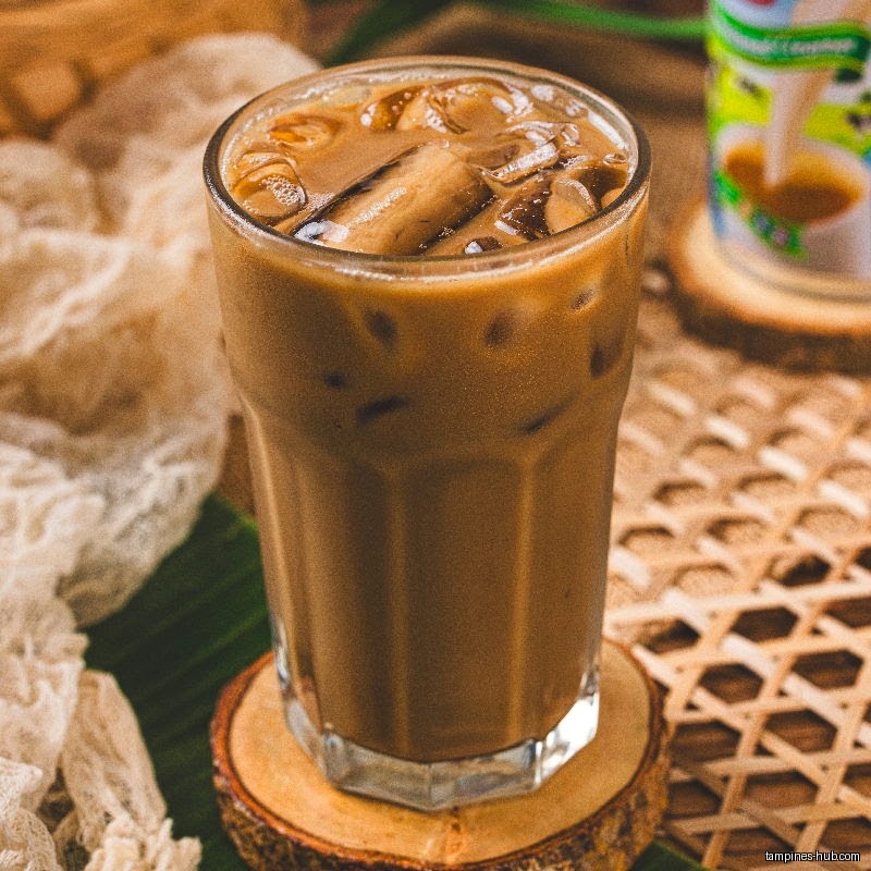 A glass of iced coffee sits on a wooden coaster and woven mat.