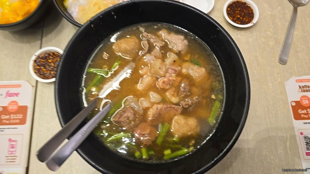 A bowl of Thai soup with meat and vegetables is on the table.