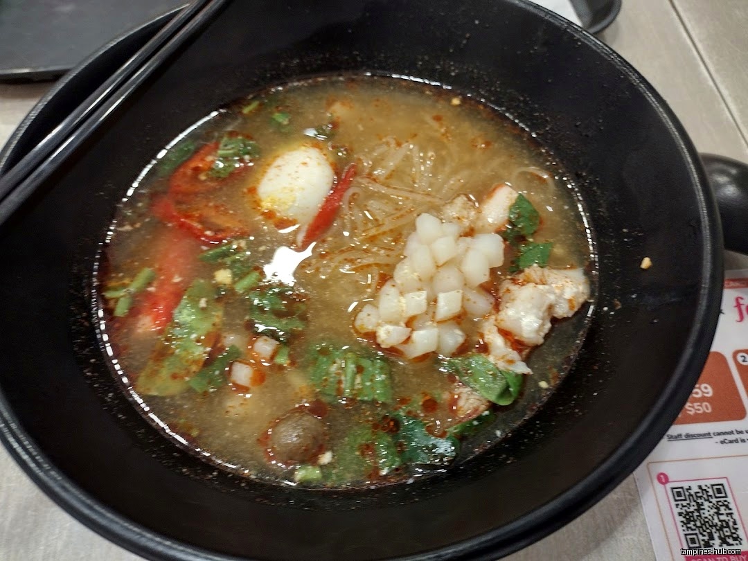 A bowl of Thai noodle soup with various ingredients and chopsticks.