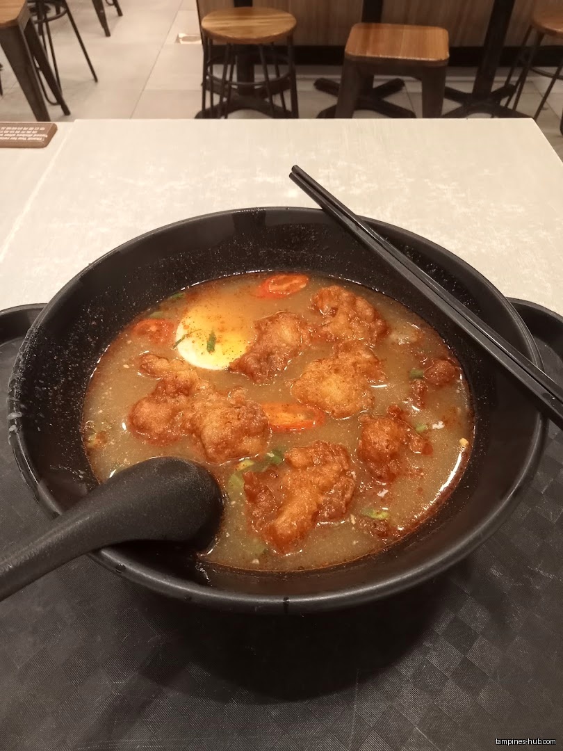 A bowl of Thai noodle soup with fried chicken and a boiled egg.