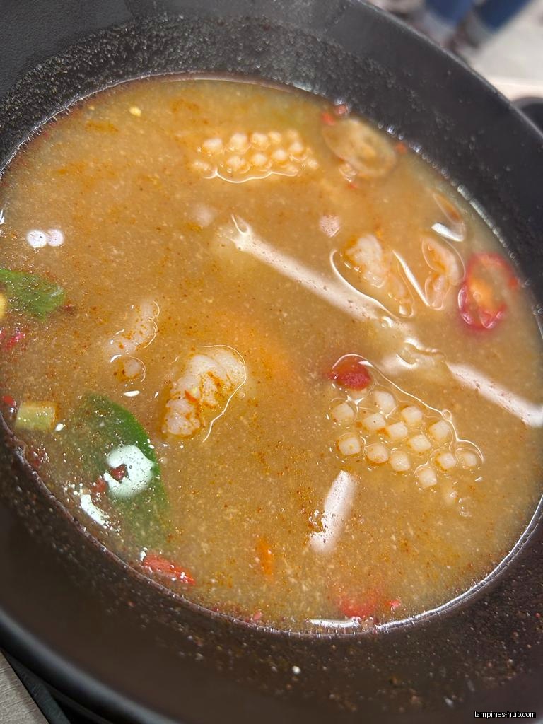 A bowl of Thai soup with shrimp and other ingredients.