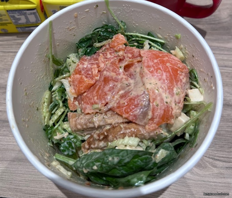 A bowl of salad with salmon, spinach, and other ingredients.