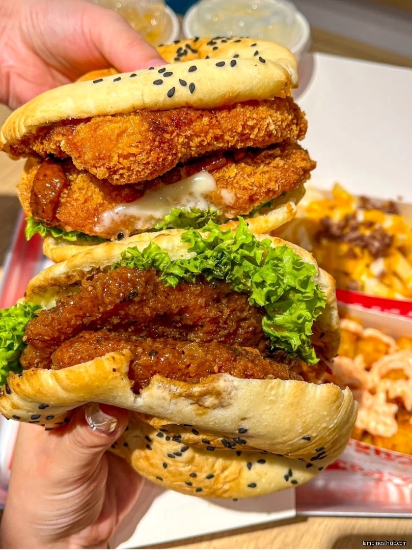 A person holds two Shiok Burgers with lettuce and sesame seed buns.