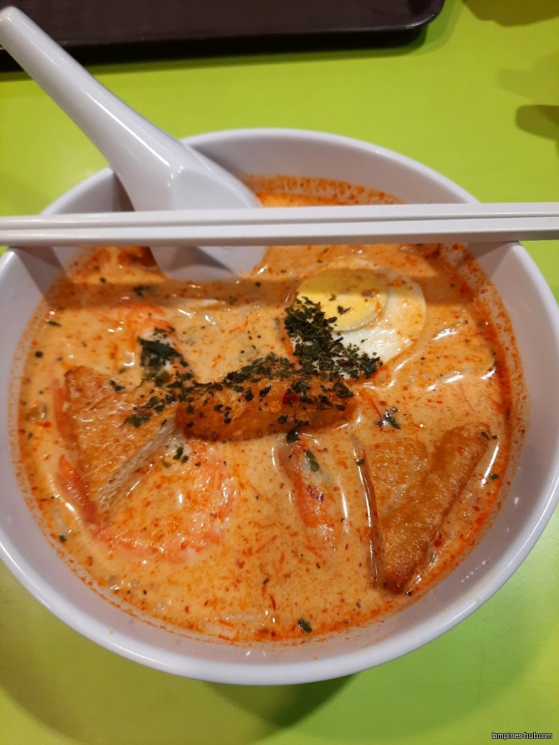 A bowl of laksa with tofu, egg, and a creamy orange broth.