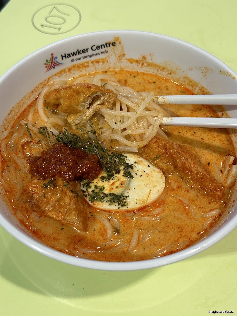 A bowl of Laksa with noodles, tofu, egg, and spicy sauce.