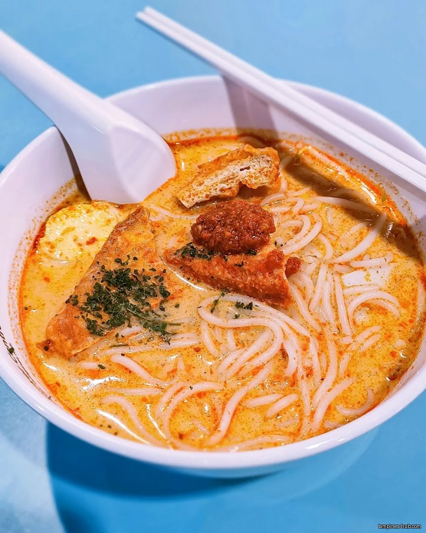 A bowl of laksa with noodles, tofu, and a creamy orange broth.