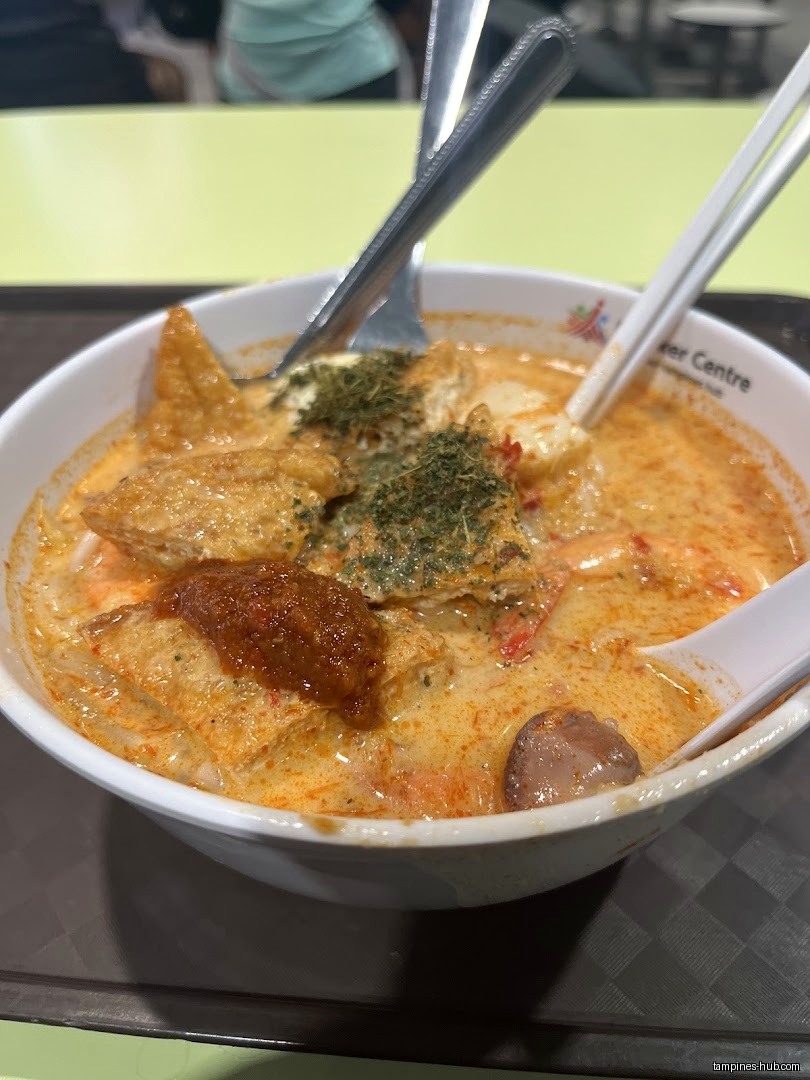 A bowl of laksa soup with tofu, herbs, and chili paste.