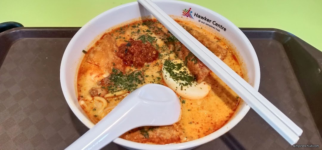 A bowl of Laksa soup with chopsticks and a spoon on a tray.