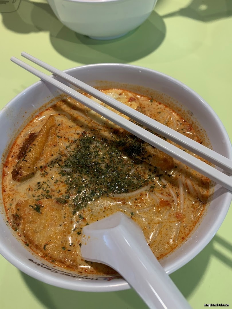 A bowl of laksa with chopsticks and a spoon is shown.