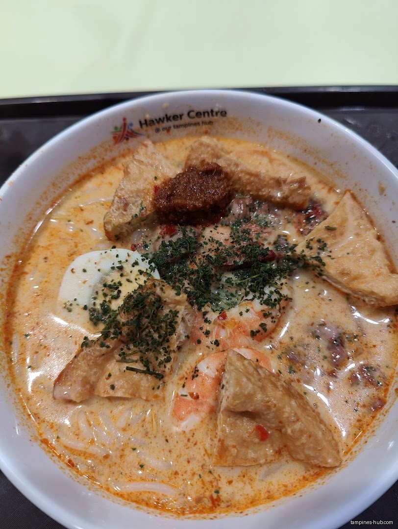 A bowl of Laksa with tofu, shrimp, egg, and herbs.