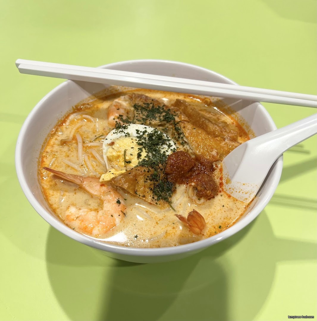A bowl of laksa with shrimp, tofu, egg, and noodles.