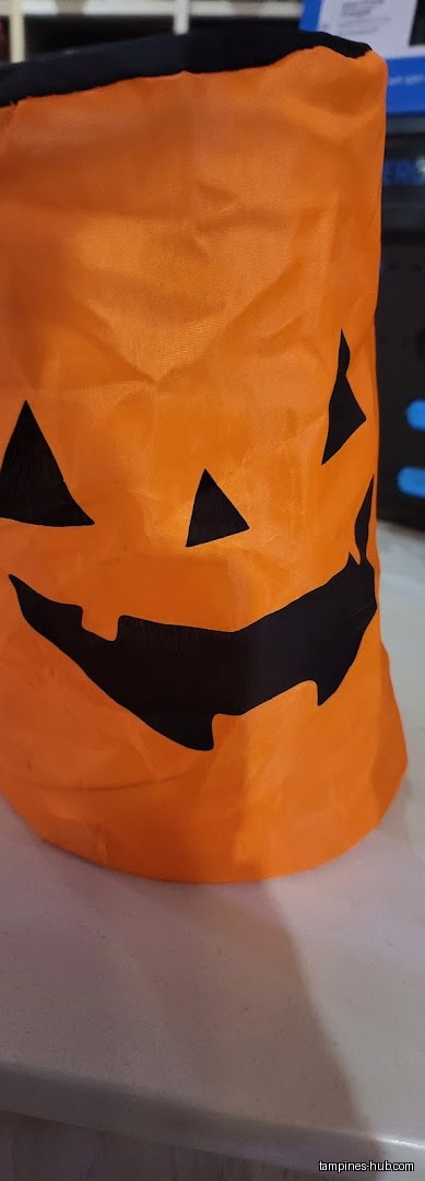 A close-up of an orange Halloween pumpkin bag with a black face.