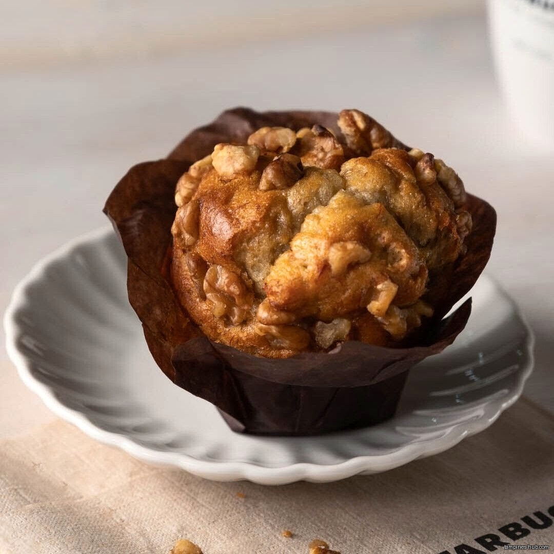 A walnut muffin in a paper cup sits on a white plate.
