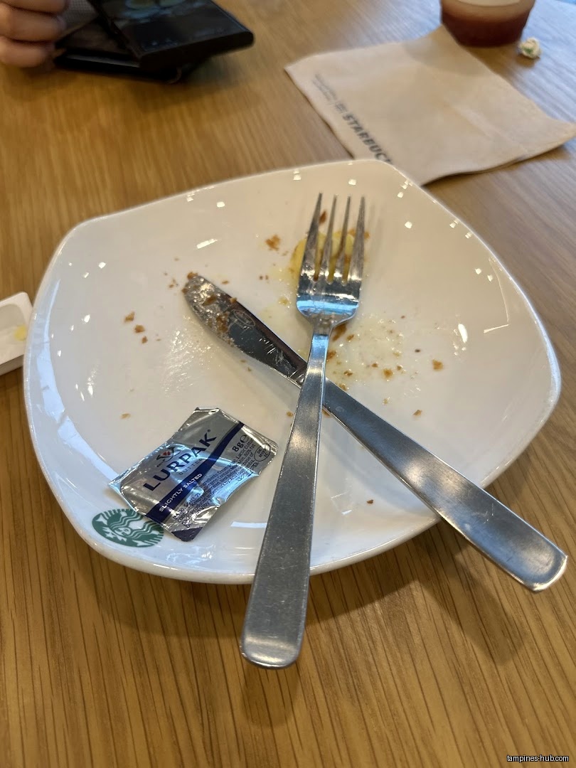 Empty plate with cutlery and Lurpak butter packet on a wooden table.