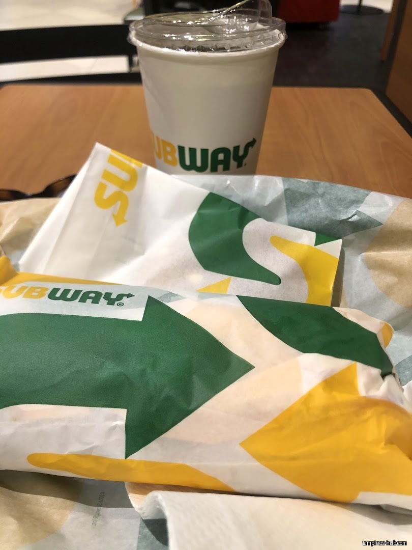 A Subway sandwich and a drink are on a table.