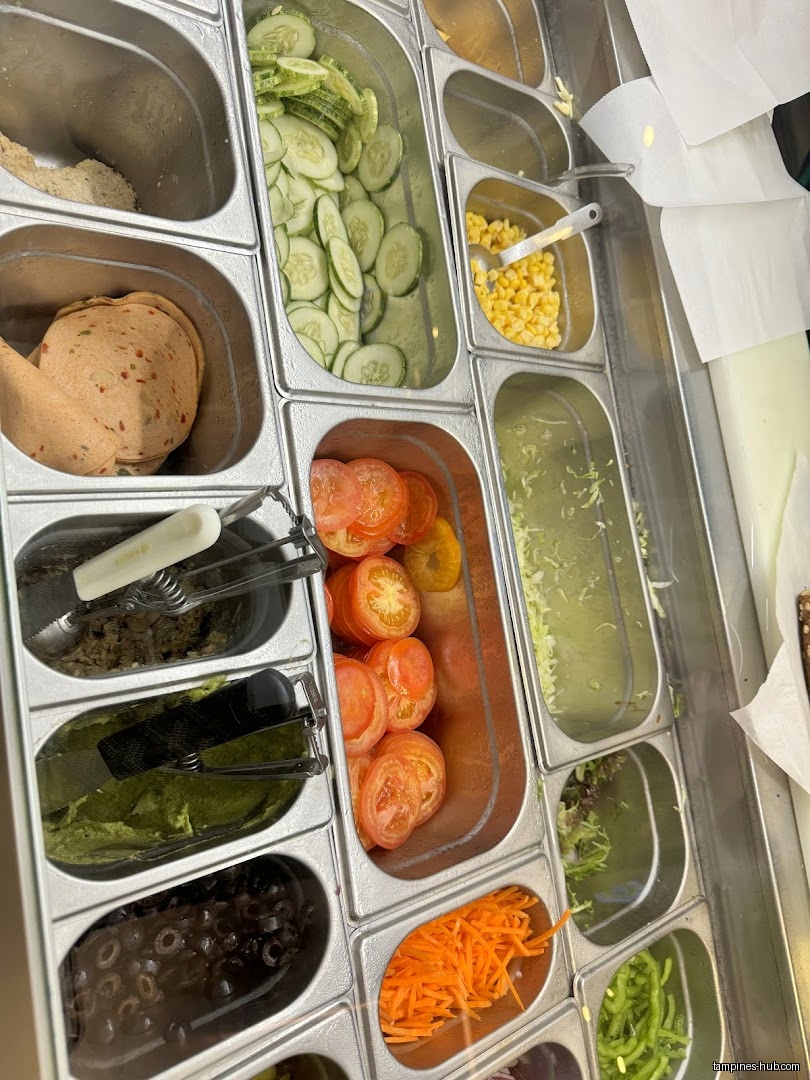 A variety of fresh sandwich toppings are displayed in metal containers.