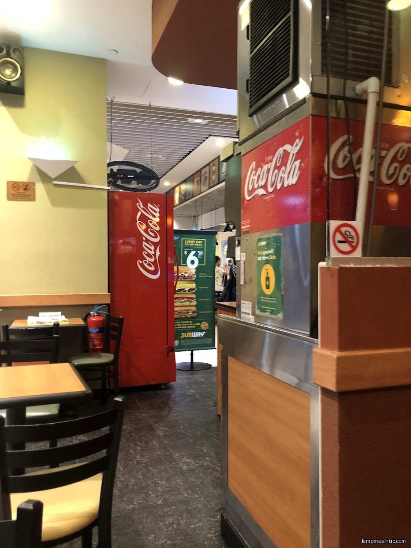 Interior view of a Subway restaurant with tables and a Coca-Cola fridge.