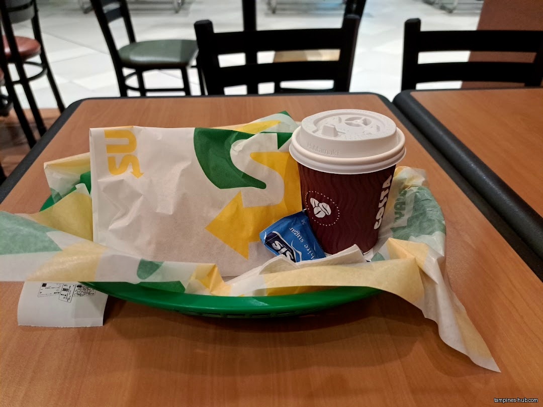 A Subway sandwich and Costa coffee sit on a table in a basket.