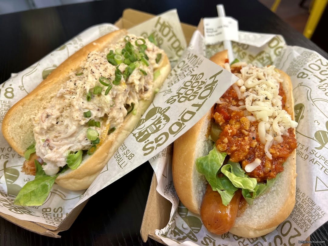 Two hotdogs with different toppings are displayed on branded paper liners.