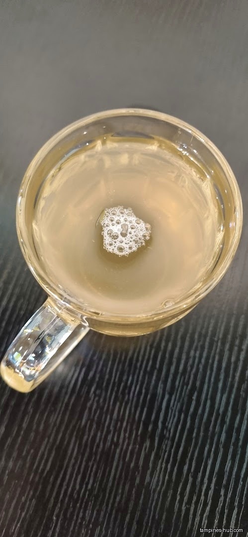 A clear glass mug filled with a light-colored liquid and bubbles.