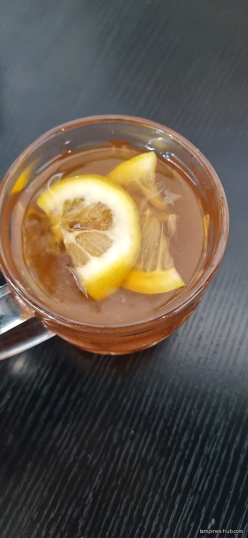A glass mug of tea with lemon slices on a dark surface.