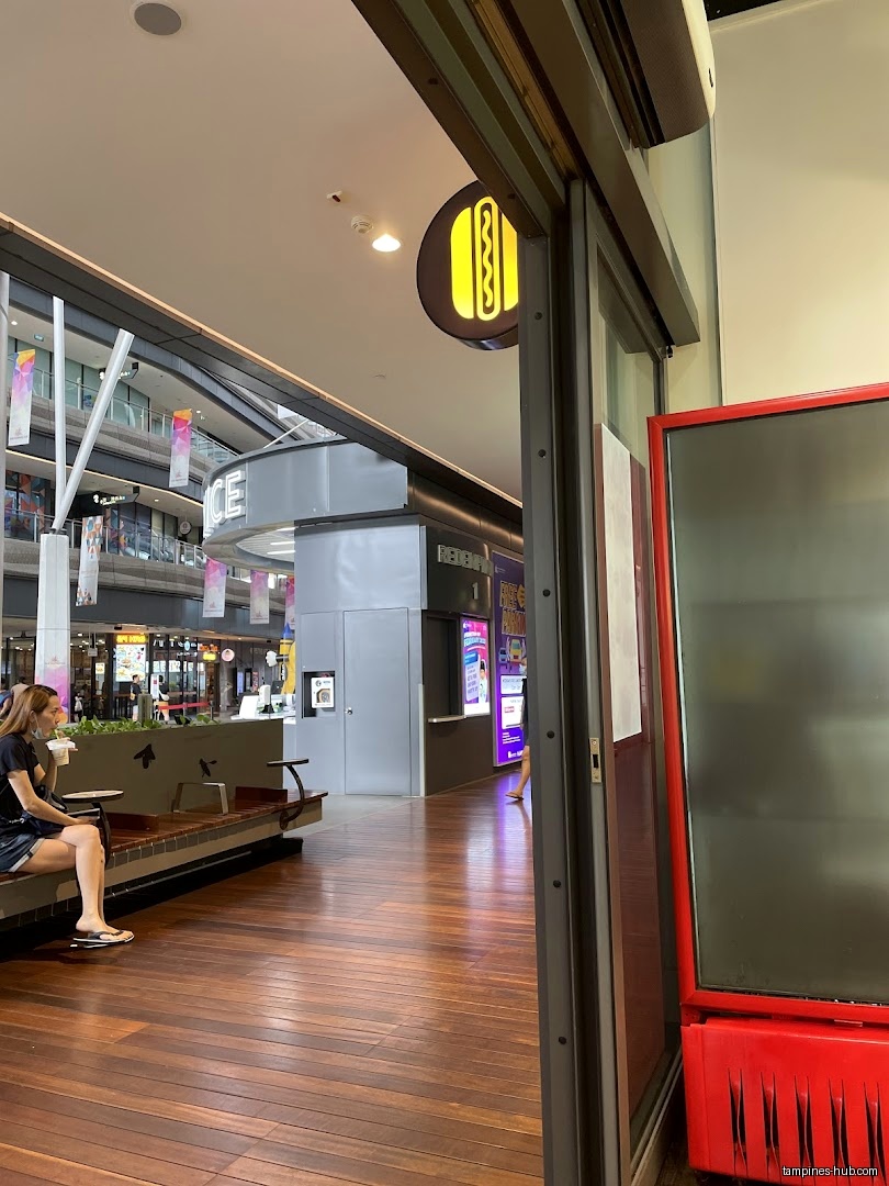 View of a shop entrance with a hotdog logo and seating area.