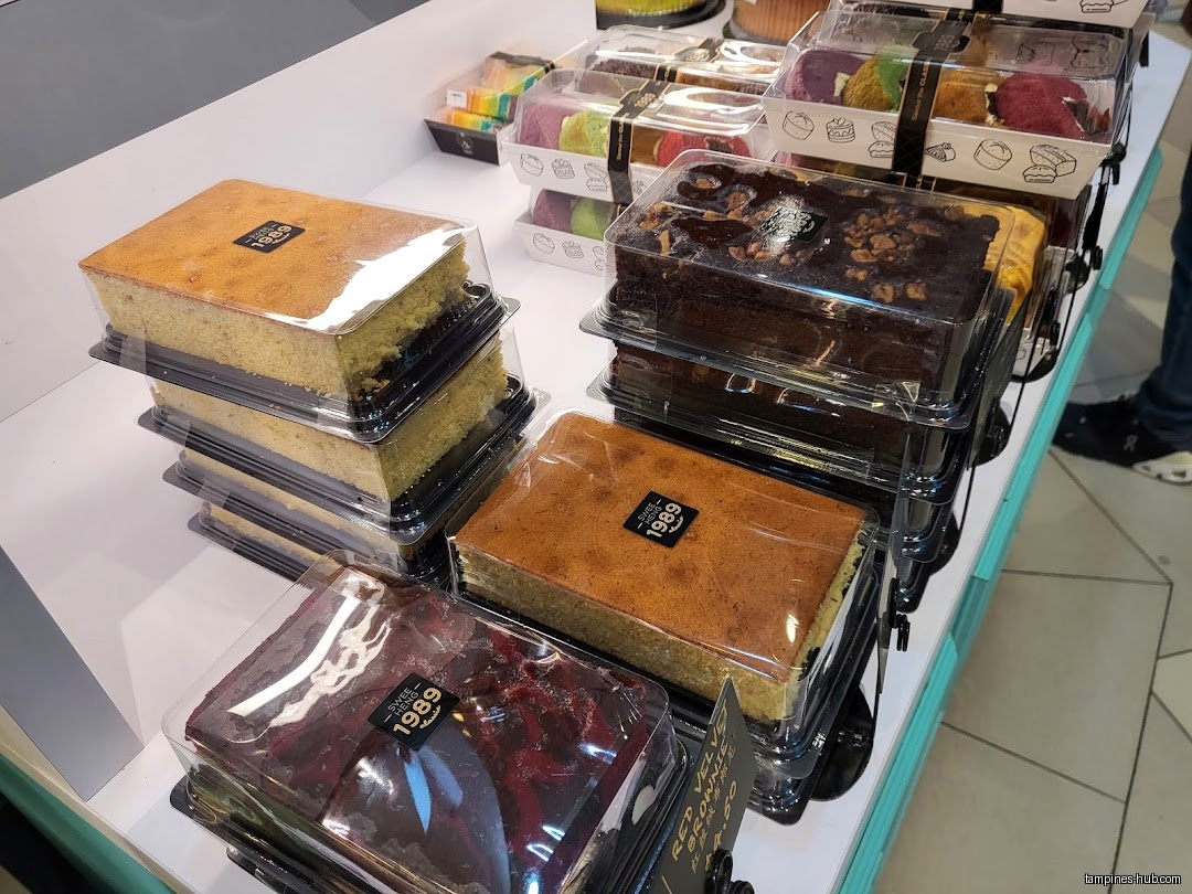 Cakes and brownies in plastic containers are displayed on a shelf.