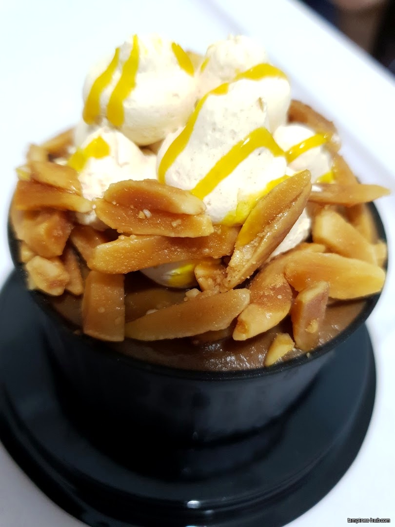 A dessert with almonds, cream, and yellow drizzle in a black cup.
