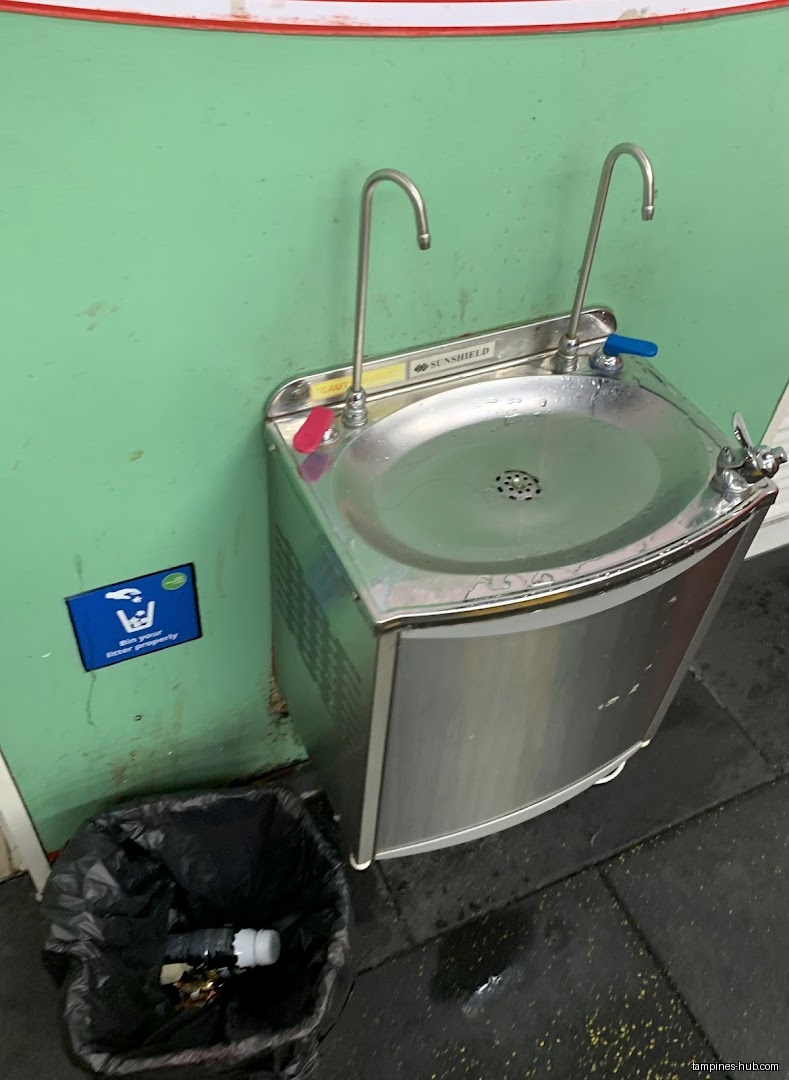 The image shows a water fountain and a trash can in a gym.