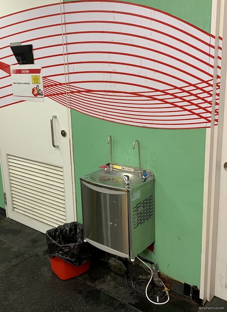 A water fountain and trash can are next to a door in a gym.