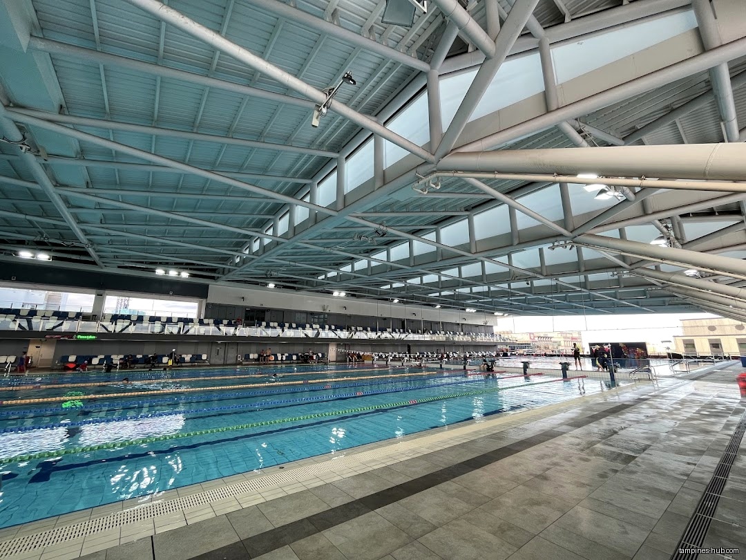 The image shows an indoor swimming pool with lanes and spectator seating.